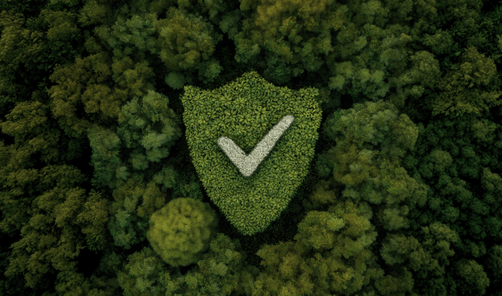 Aerial view of a green shield and checkmark formed by leaves, surrounded by dense forest foliage. Symbolizes environmental assurance.