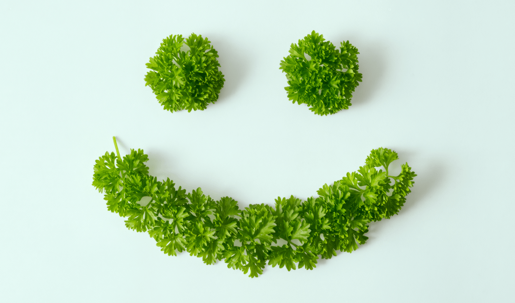 A smiley face created from bright green parsley leaves on a light background, with circular shapes for eyes and a curved mouth.