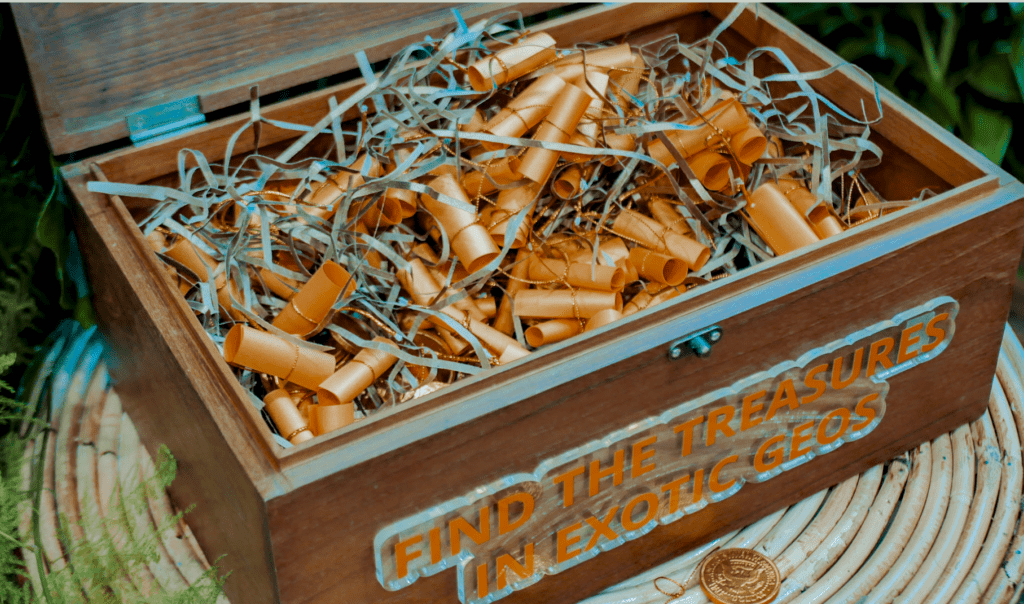 A wooden treasure chest filled with golden scrolls and decorative shreds, featuring the text "FIND THE TREASURES IN EXOTIC GEOS."