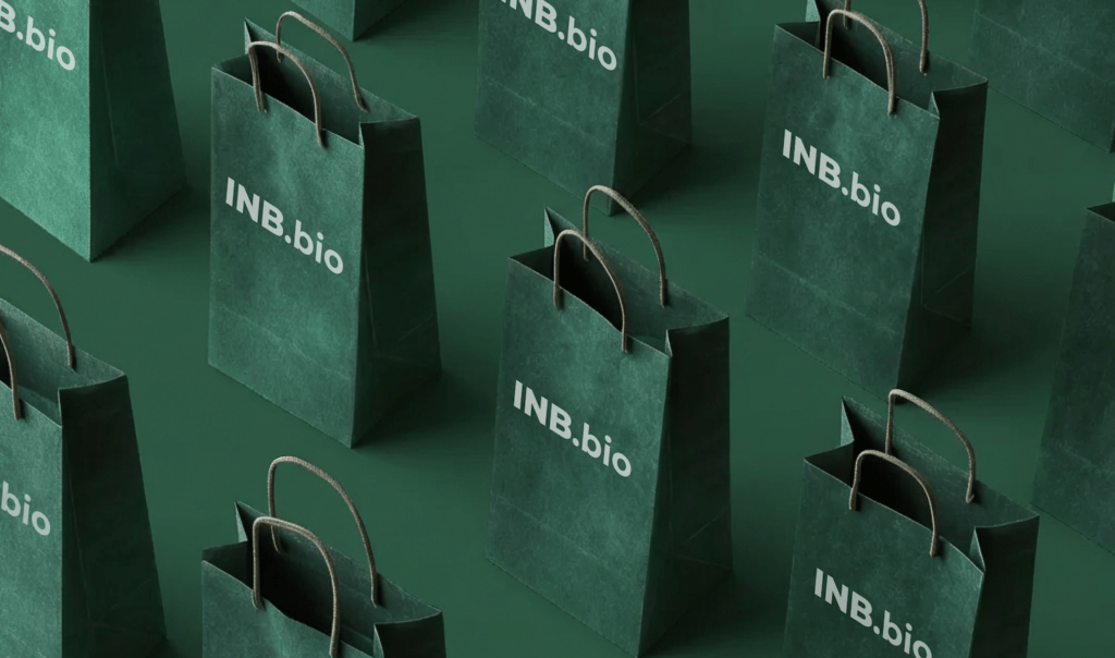 A flat lay of green paper bags with the logo "INB.bio" prominently displayed in white on each bag.