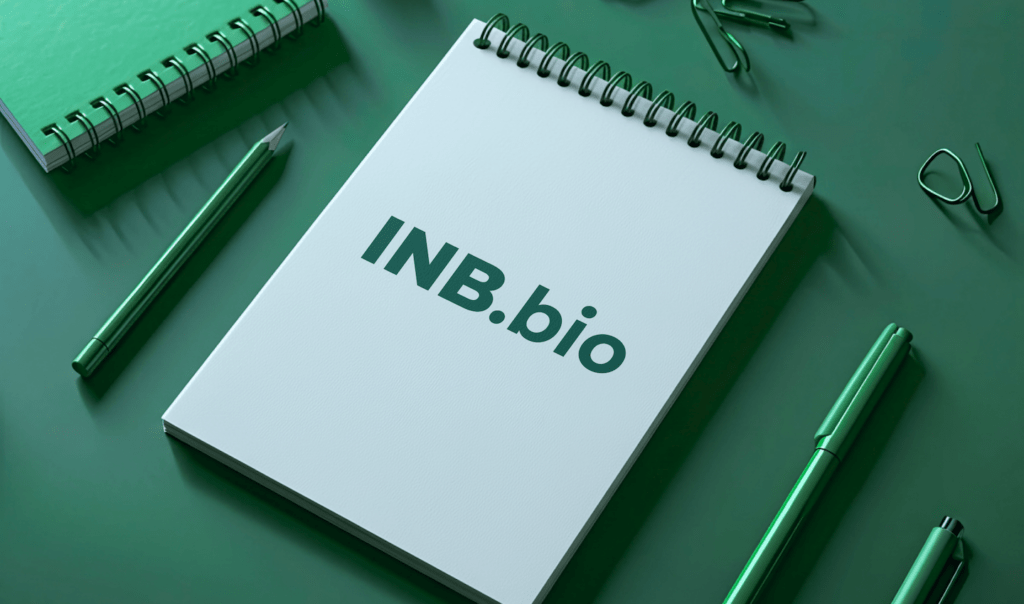 A flat lay of a white spiral notebook displaying "INB.bio," green pens, and stationery items on a green background.