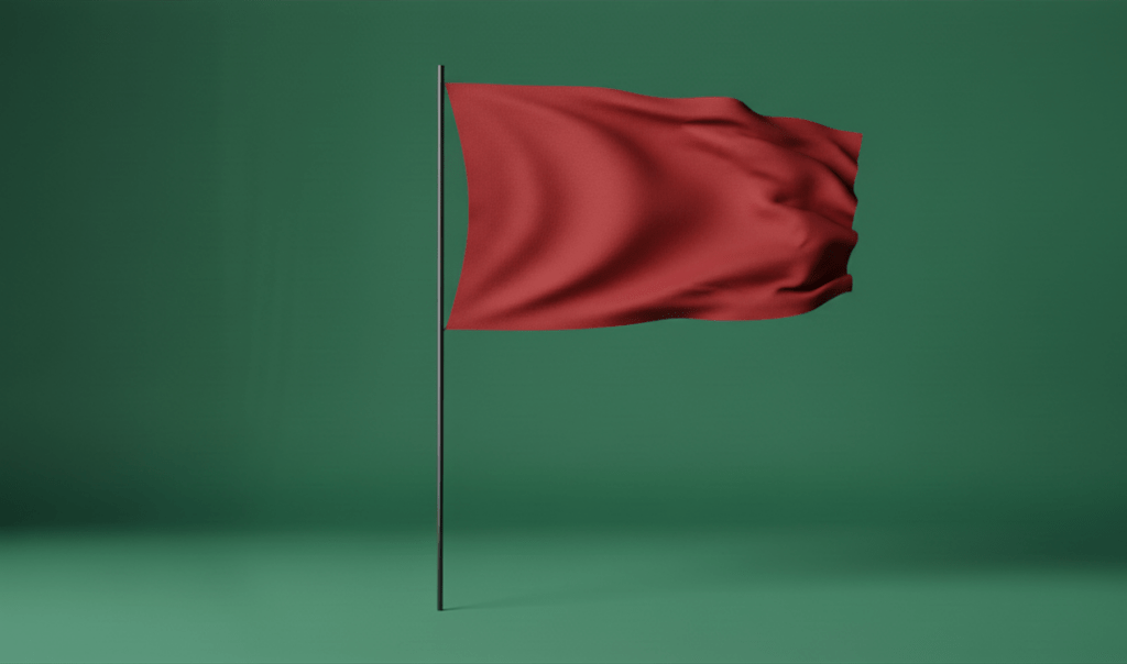 A red flag gently waving on a black pole against a green background.