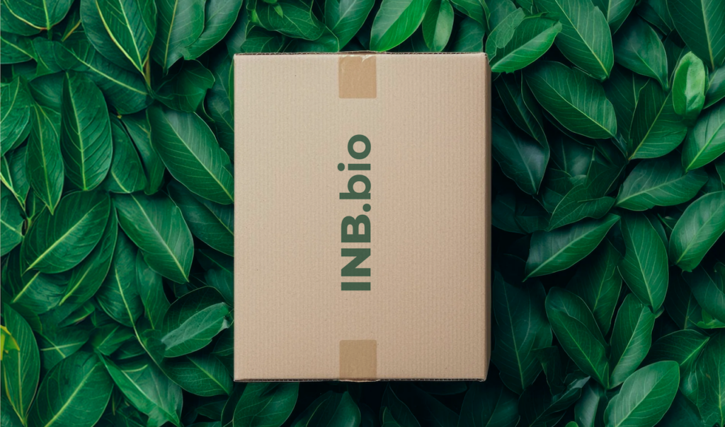 Cardboard box with "INB.bio" text, placed on a lush green leaf background, symbolizing eco-friendly packaging.