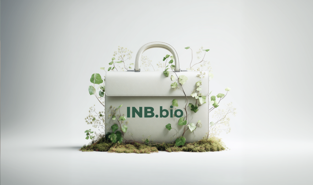White leather handbag with "INB.bio" text, surrounded by green leaves and moss on a light background.